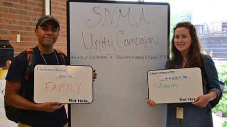 Two students holding whiteboard signs. The sign on the left says 'Charlottesville is a place for family, not hate'. The sign on the right says 'Charlottesville is a place for solidarity, not hate'.